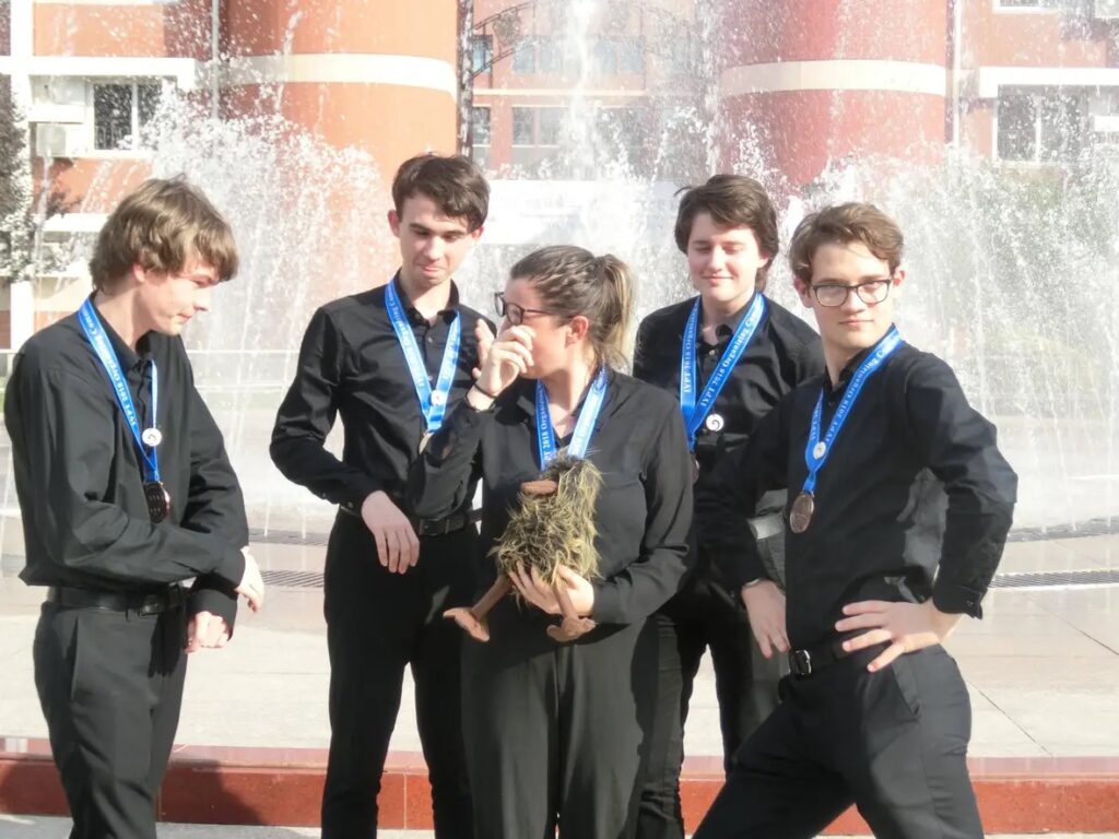 The 2018 NZ rep team after their bronze medal photoshoot with Luke posing for the camera alongside teammates Zoë Danger Mansell, Finnegan Messerli, Zuni Preece, Ensai August and mascot Ernie (Rutherford) the kiwi. 